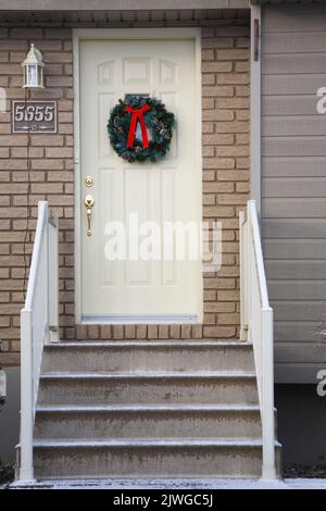 Fassade eines kleinen Bungalows mit einem Weihnachtskranz vor der Tür. Stockfoto