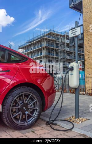 Ein rotes Tesla-Auto lädt seine Autobatterie an einer Ladestation für Elektrofahrzeuge in Southampton, England, Großbritannien Stockfoto