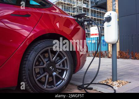 Ein rotes Tesla-Auto lädt seine Autobatterie an einer Ladestation für Elektrofahrzeuge in Southampton, England, Großbritannien Stockfoto