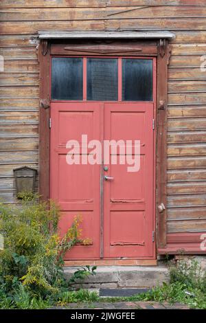 Alte rote Holztüren, Eingang zum Holzhaus mit verdorrter abblätternder Farbe an den Wänden. Tartu, Estland. Stockfoto