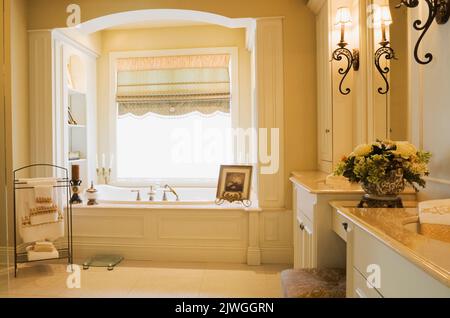 Modernes Badezimmer mit Wanne mit Holzpaneelen und weißen hölzernen Kosmetikbereichen in einem üppig dekorierten und luxuriösen Haus im Cottage-Stil. Stockfoto
