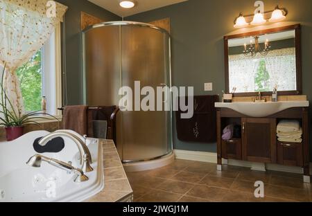 Hauptbadezimmer mit Whirlpool-Badewanne, Glasduschkabine und Waschbecken aus Porzellan im modernen Haus im Landhausstil. Stockfoto