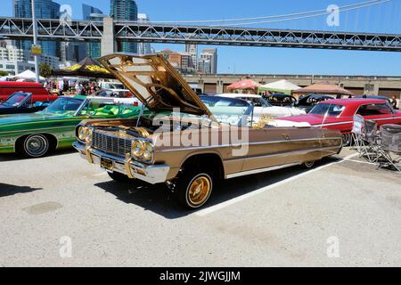 1964 Chevy Impala Lowrider Cabriolet in Braun mit goldener Zierleiste; Lowrider-Autokultur auf einer Automobilausstellung im Embarcadero in San Francisco, Kalifornien. Stockfoto