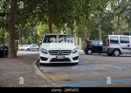 Weißer Mercedes Benz C180 auf einem öffentlichen Parkplatz neben einem Park an einem bewölkten Tag Stockfoto