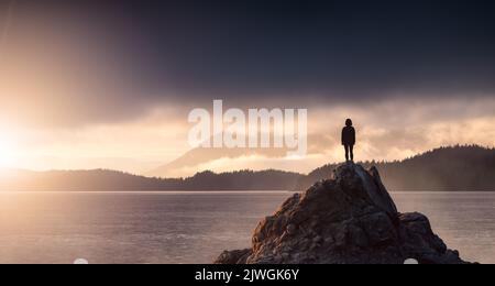 Abenteuerliche Frau Wandern an der Rocky Coast mit Bergen und dramatischem Sonnenuntergang Himmel. Stockfoto