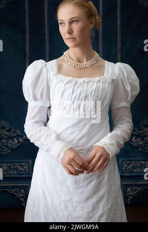 Eine Regency-Frau, die ein weißes, besticktes Musselin-Kleid mit Perlenkette trägt Stockfoto