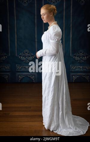 Eine Regency-Frau, die ein weißes, besticktes Musselin-Kleid mit Perlenkette trägt Stockfoto