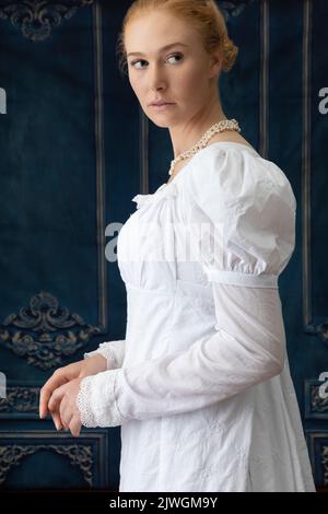 Eine Regency-Frau, die ein weißes, besticktes Musselin-Kleid mit Perlenkette trägt Stockfoto