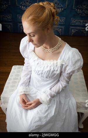 Eine Regency-Frau, die ein weißes, besticktes Musselin-Kleid mit Perlenkette trägt Stockfoto