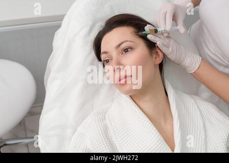 Der Arzt macht eine Injektion in den Kopf eines Mädchens aus Haarausfall. Haarbehandlung in einer Kosmetikklinik. Stockfoto