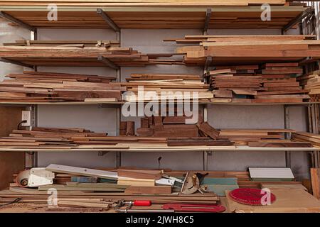 Holzwerkstatt mit Regalen, die Holzteile, Bretter an der Wand und einige Handwerkzeuge auf dem Tisch halten Stockfoto