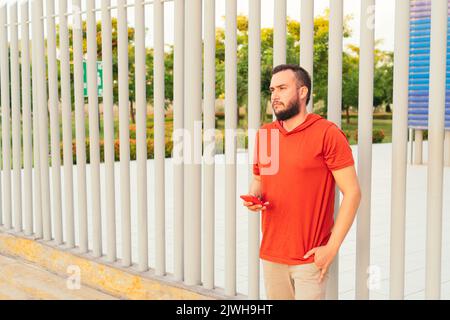 Bärtiger junger Mann, der an einem sonnigen Tag sein Handy im Park überprüft. Stockfoto