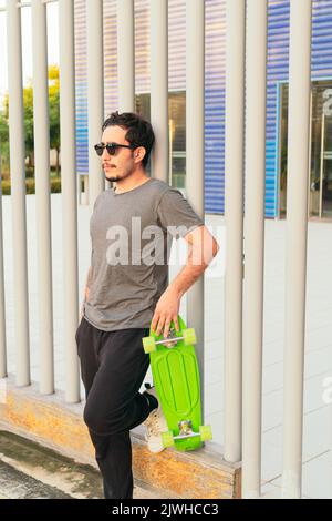 Hispanic Mann mit Sonnenbrille und Skateboard im Park an einem sonnigen Tag. Stockfoto