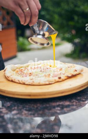 Fertig heiße Pizza wird Sauce gegossen. Der Prozess der Herstellung von hausgemachter Pizza. Das Konzept der hausgemachten Fast Food. Vertikales Foto. Stockfoto