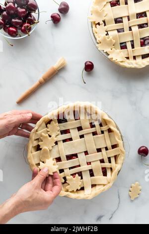 Vorbereiten von Kirschkuchen zum Backen mit den Händen auf dekorative Blätter setzen. Stockfoto