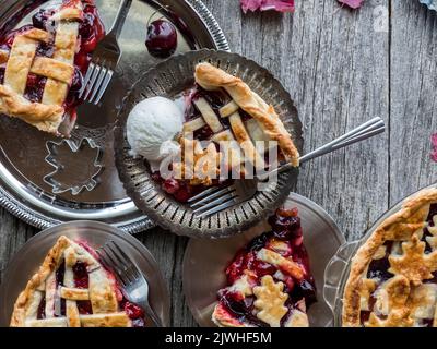 Kirschkuchenscheiben auf glänzenden Metallplatten auf einem rustikalen Holzbrett. Stockfoto