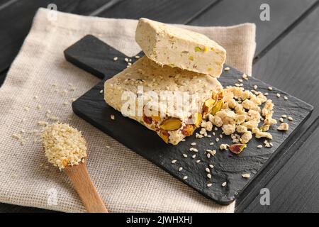 Tafel mit leckeren Sesamhalva mit Pistazien auf dunklem Holzhintergrund Stockfoto