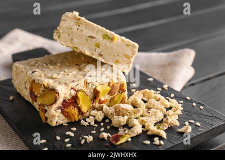 Tafel mit leckeren Sesamhalva mit Pistazien auf dunklem Holztisch, Nahaufnahme Stockfoto