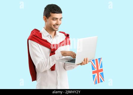 Junger Mann mit britischer Flagge mit Laptop auf blauem Hintergrund Stockfoto
