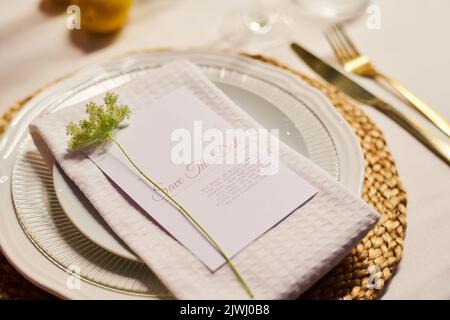 Nahaufnahme eines weißen Porzellantellers mit gefalteter Baumwollserviette und einer kleinen grünen Zierpflanze über der Karte mit Text auf dem geservierten Tisch Stockfoto