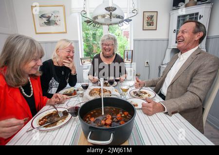 Eine Gruppe von Leuten, die zu Hause eine Abendparty feiern. Fröhliche Freunde, die am Esstisch sitzen, essen und reden Stockfoto