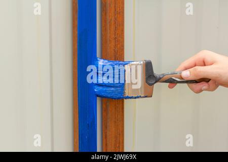 Rost mit blauer Farbe für Metall malen.die Hand malt die Querstreben des Zauns Stockfoto