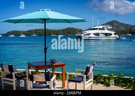 Die Yasawa Flyer-Fähre bringt Passagiere im Nanuya Island Resort mit Sonnenschirm und Tisch und Stühlen im Vordergrund ab. Fidschi Stockfoto