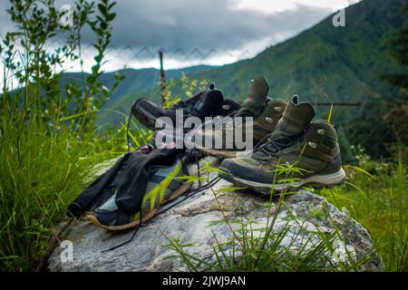 Juli 21. 2021. Uttarakhand Indien. Paar Trekkingschuhe und Socken auf einem Felsen mit Landschaften und Himmel im Hintergrund. Stockfoto