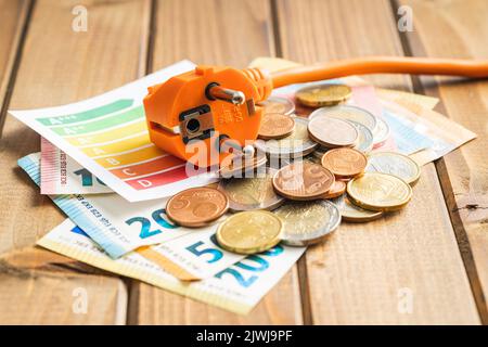Elektrostecker, Euro-Geld- und Energieetikett auf dem Holztisch. Konzept der steigenden Strompreise. Stockfoto