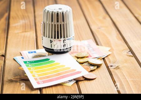 Thermostat-Ventilkopf, Euro-Geld- und Energieetikett auf dem Holztisch. Konzept der steigenden Strompreise. Stockfoto