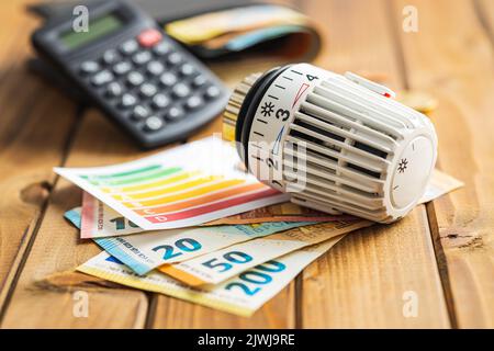 Thermostat-Ventilkopf, Euro-Geld- und Energieetikett auf dem Holztisch. Konzept der steigenden Strompreise. Stockfoto