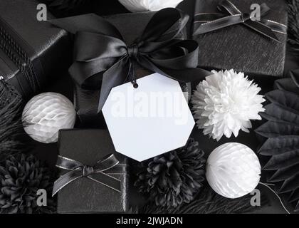 Geschenkboxen mit schwarzen und weißen Papierblumen und Dekorationen, quadratischen Geschenkanhänger Mockup, Kopierraum. Dunkle Komposition mit leerer Etikettenkarte für Christma Stockfoto