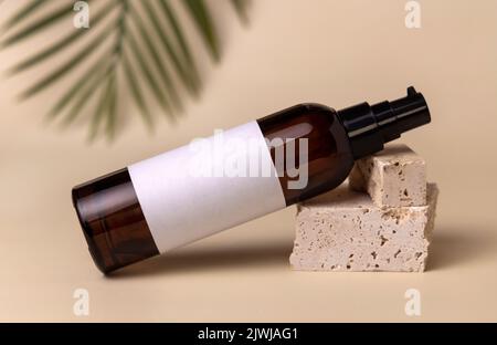 Glaskosmetikflasche mit einer Pumpe auf Stein auf hellbeige mit einem Palmblatt, Nahaufnahme, Etikettenmockup. Hautpflegeprodukt, Lotion oder Essenz. Natürliche c Stockfoto