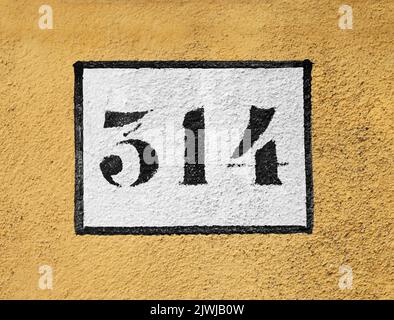 Nahaufnahme weißes Rechteck mit 314 Nummer und schwarzer Umrisse auf gelber Gebäudewand gemalt Stockfoto