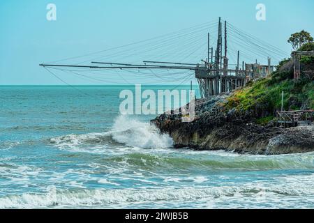 Die Wellen kollidieren auf den Klippen der apulischen Küste. Ein Baumstäbchen steckt seine Netze in das raue Meer. Vieste, Provinz Foggia, Apulien, Italien, Europa Stockfoto