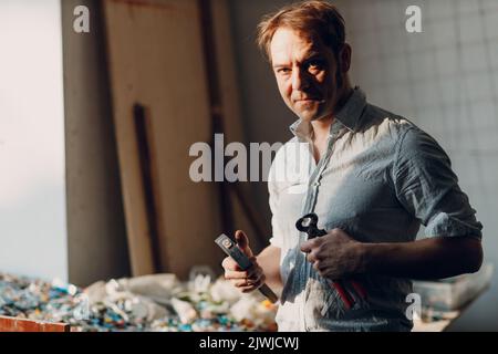 Handwerker männliche Meister Porträt halten Hammer und Smaltglas Stücke in Arm Hand für Mosaik-Kunstwerk in der Werkstatt. Stockfoto