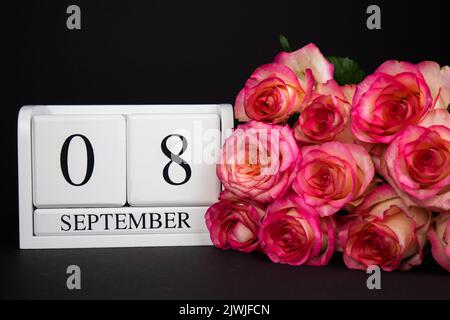 September 8 Holzkalender, weiß auf schwarzem Grund, rosa Rosen liegen in der Nähe. Stockfoto