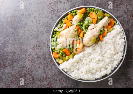 Hähnchendrumsticks, geschmort mit Karotten und grünen Erbsen, serviert mit Reis aus nächster Nähe auf einem Teller auf dem Tisch. Horizontale Draufsicht von oben Stockfoto