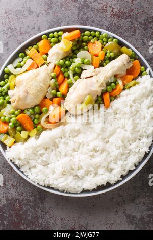 Erbsen und Karotten Hähncheneintopf Pollo Arvejado mit Reis garnieren, in der Nähe auf dem Teller auf dem Tisch. Vertikale Draufsicht von oben Stockfoto