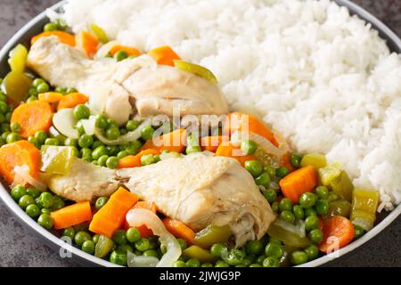 Hähnchendrumsticks, geschmort mit Karotten und grünen Erbsen, serviert mit Reis aus nächster Nähe auf einem Teller auf dem Tisch. Horizontal Stockfoto