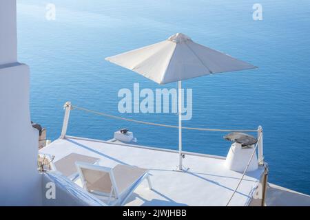 Griechenland. Terrasse mit Meerblick an einem sonnigen Tag auf Santorini. Ein Paar Sonnenliegen und ein Sonnenschirm Stockfoto