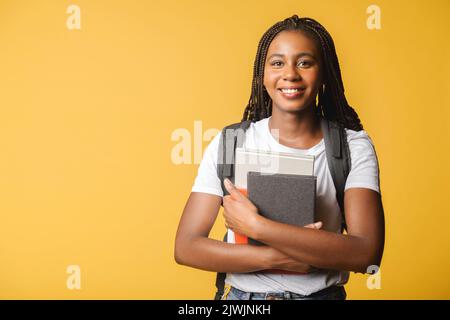 Glücklich aufgeregt Studentin mit Rucksack isoliert auf gelb stehen und hält Bücher und Abstracts, bereit zum Studium, zurück zur Schule Konzept Stockfoto