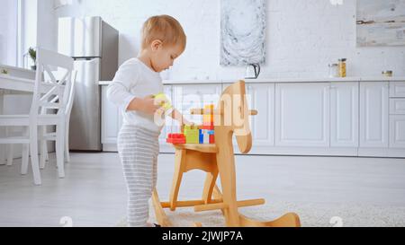 Kleinkind Kind spielt mit Bausteinen auf Schaukelpferd in geräumigen Wohnung Stockfoto