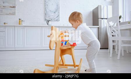 Liebenswert Kleinkind Kind spielt mit Kunststoff-Bausteine auf Schaukelpferd in geräumigen Wohnung Stockfoto