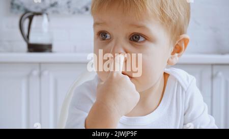 Nahaufnahme eines frechen Kleinkindes, der seine Nase pflückt und wegschaut Stockfoto