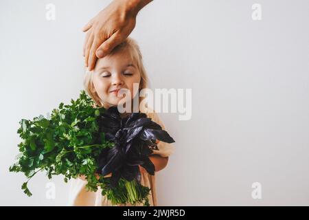 Nettes Kind Mädchen mit Koriander und Basilikum Haufen gesund essen vegane Lebensmittel Bio Ernte Bauernhof Gartenarbeit pflanzenbasierte Ernährung umweltfreundlich lebend Stockfoto