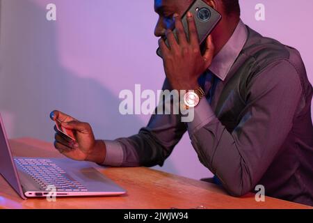 afrikanischer Geschäftsmann, der einen Anruf mit seinem Laptop und einer Kreditkarte führt Stockfoto
