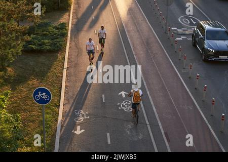 Aus der Vogelperspektive sehen Sie, wie Radfahrer und zwei männer auf Kick-Scootern auf der Fahrradstraße fahren. Konzept des aktiven Lebensstils. Stockfoto