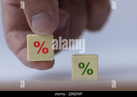 Hand hält ein Stück Scrabble mit einem grünen Prozentzeichen, das symbolisiert, dass die Zinssätze von positiv auf negativ angesetzt werden. Stockfoto