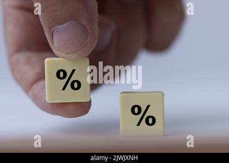 Hand hält ein Stück Scrabble mit schwarzem Prozentzeichen, das symbolisiert, dass die Zinssätze neutral sind. Stockfoto